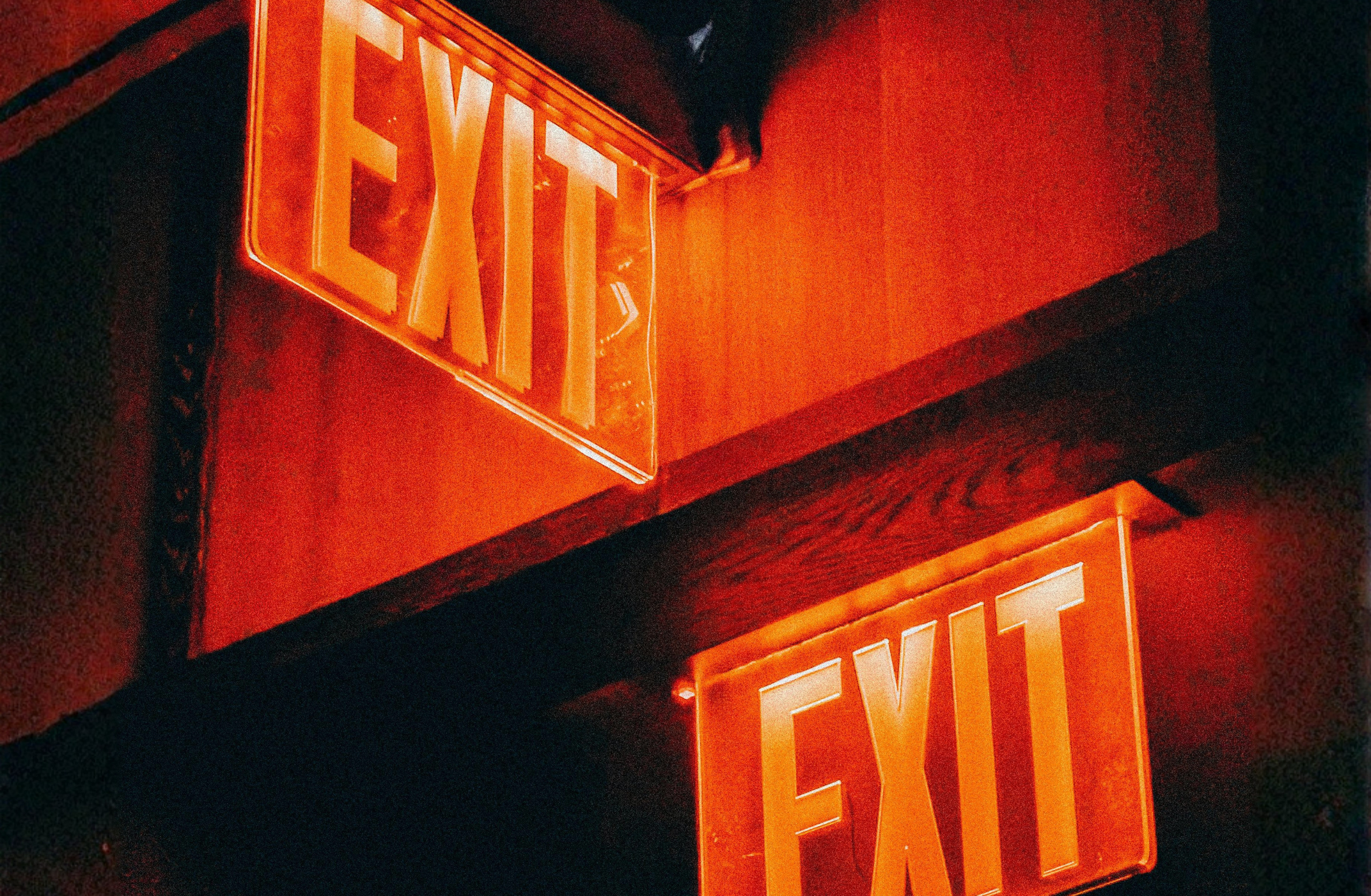 Two illuminated red exit signs inside a dark building.