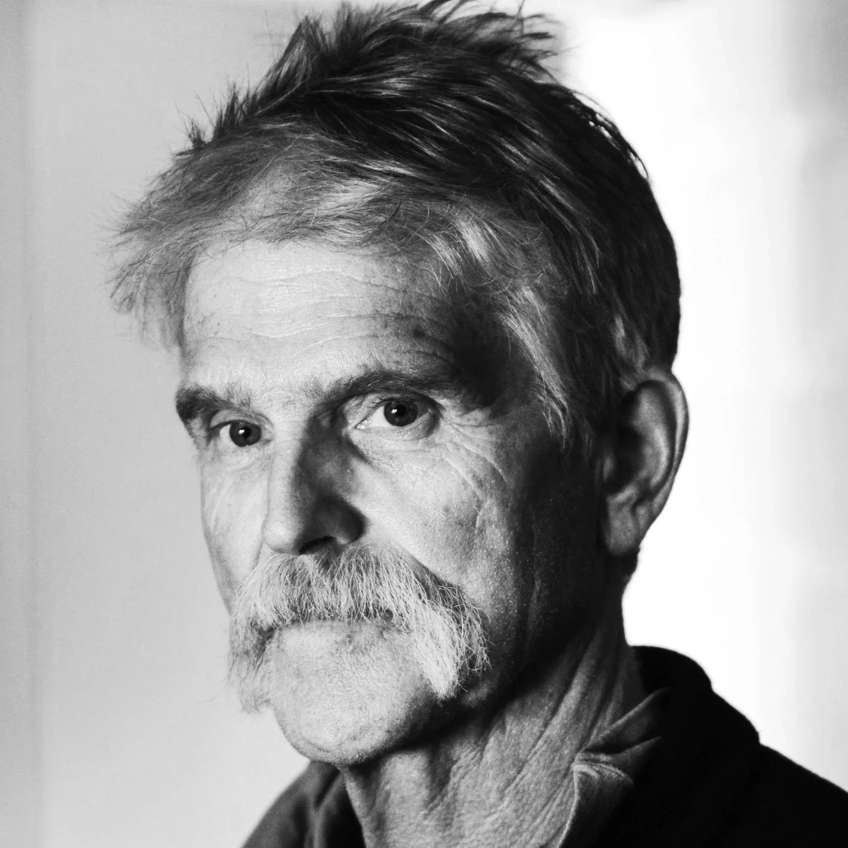 Black and white close-up portrait of a man with a beard and mustache, with short, styled hair, looking slightly to the left.
