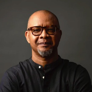 Portrait of a man with glasses and a black shirt against a dark background.