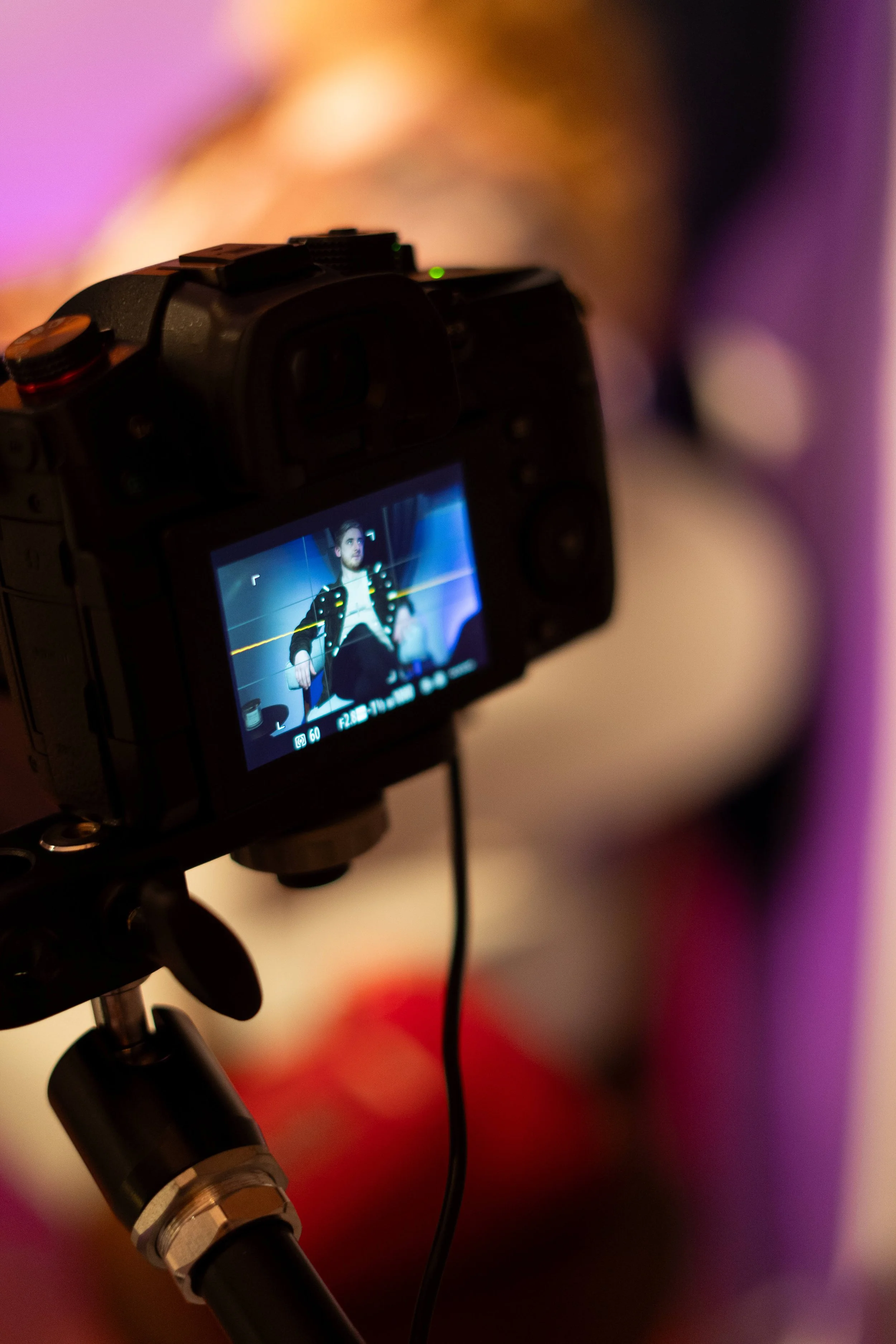 A DSLR camera mounted on a tripod, capturing a person sitting against a colorful, blurred background in a photography studio.