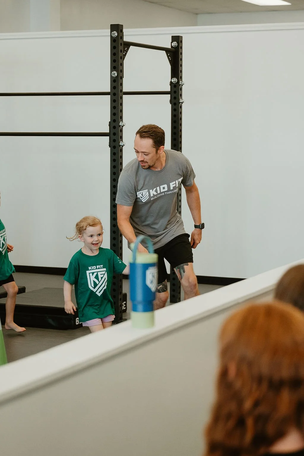 Fitness instructor and young girl in a gym, holding hands and smiling.