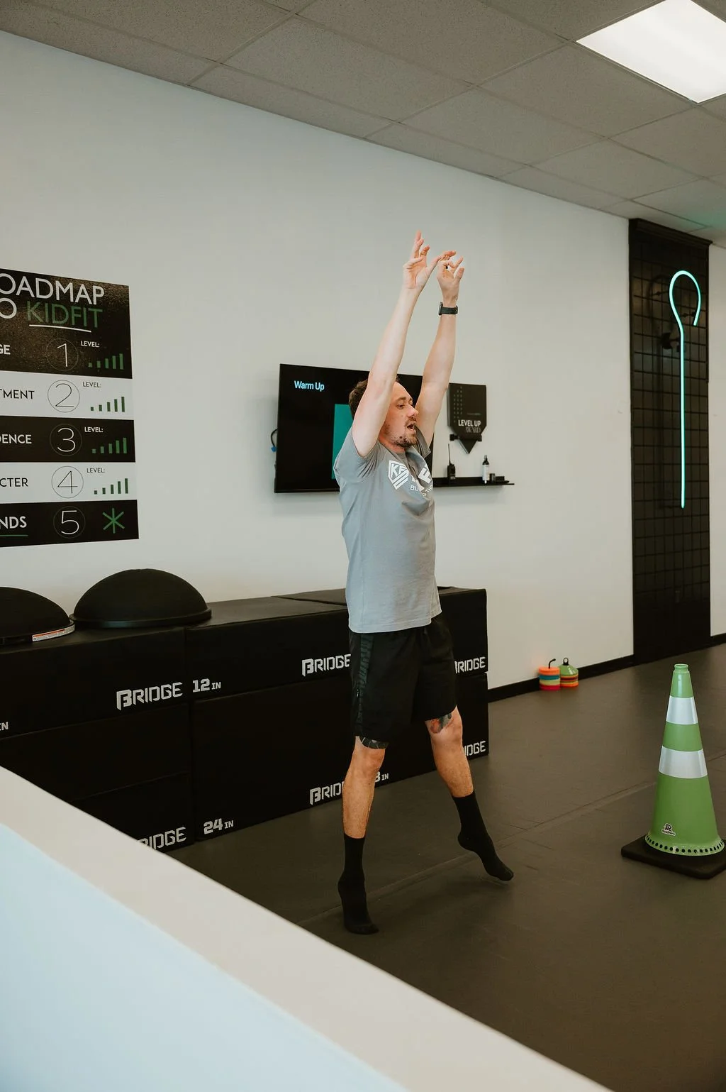 Man stretching in a gym, wearing a grey t-shirt, black shorts, and black socks.