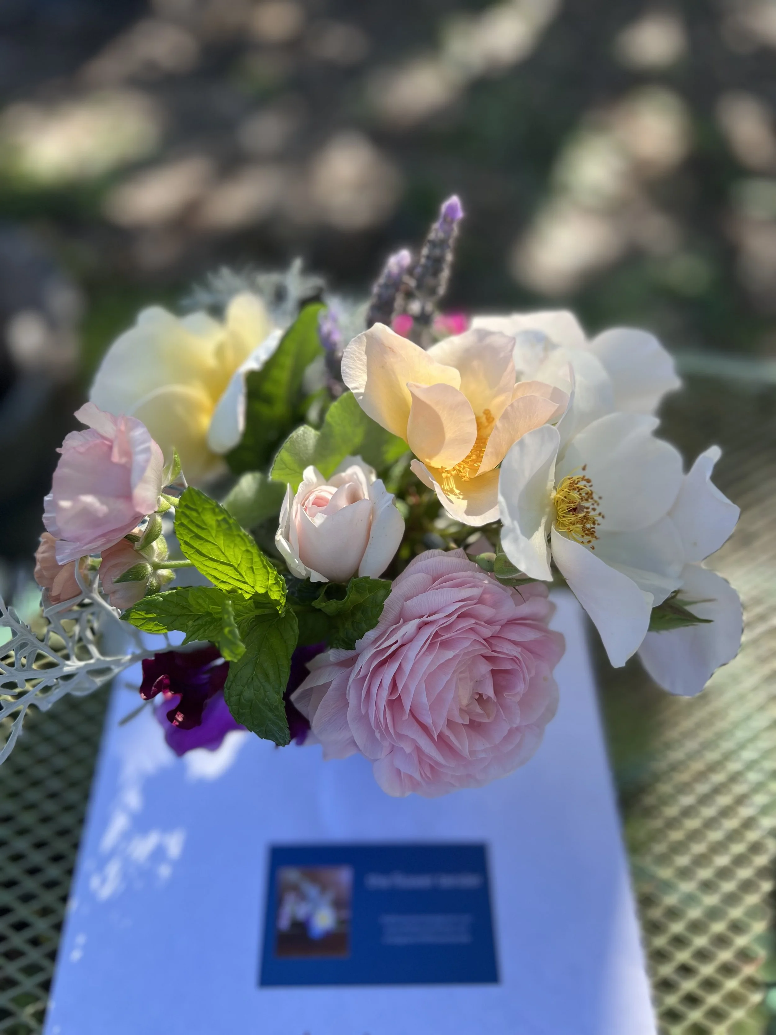 small posey of colorful pastel flowers with a blurred business card that reads: the flower tender.