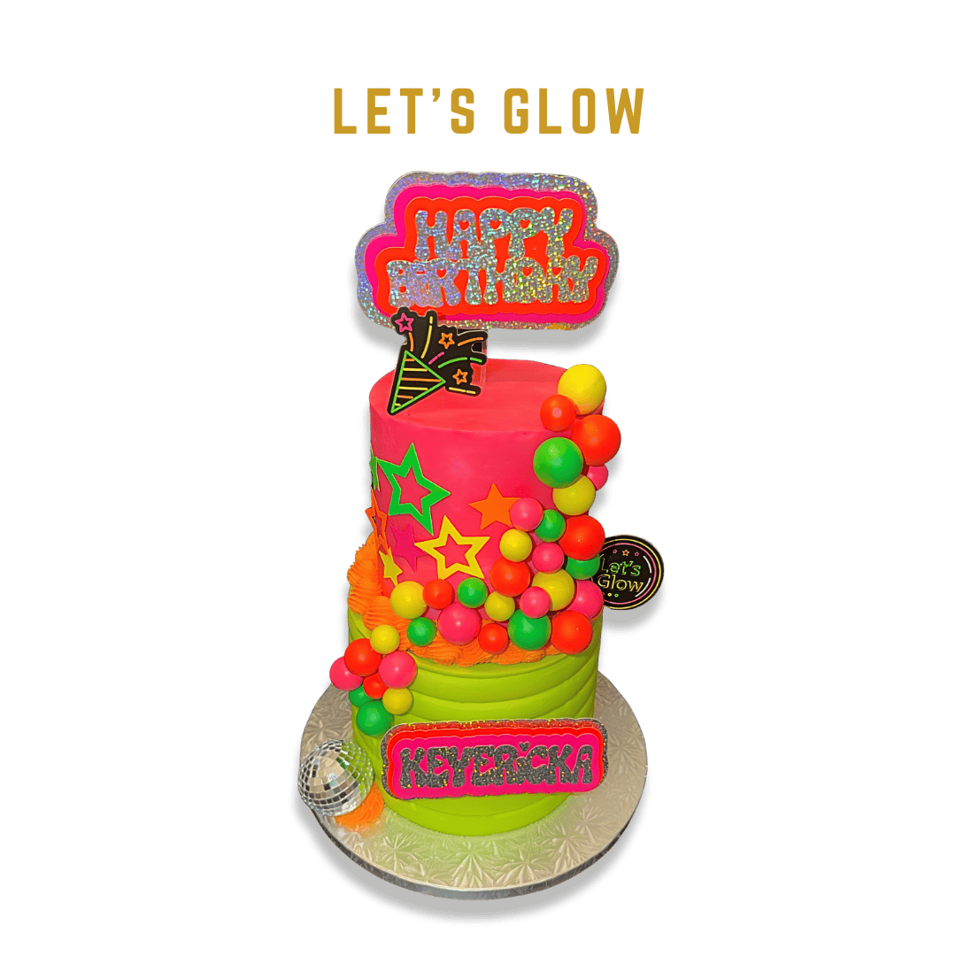 Bright pink and green birthday cake decorated with colorful jelly beans and star-shaped cutouts, topped with a glow-in-the-dark "Happy Halloween" sign, a small disco ball, and a tag reading "Let's Glow."