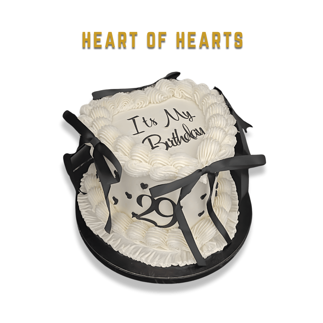 A round white birthday cake with black ribbons and a message that says "It’s My Birthday" on top, decorated with white frosting and black number "29" on the side, with the words "Heart of Hearts" above the cake.