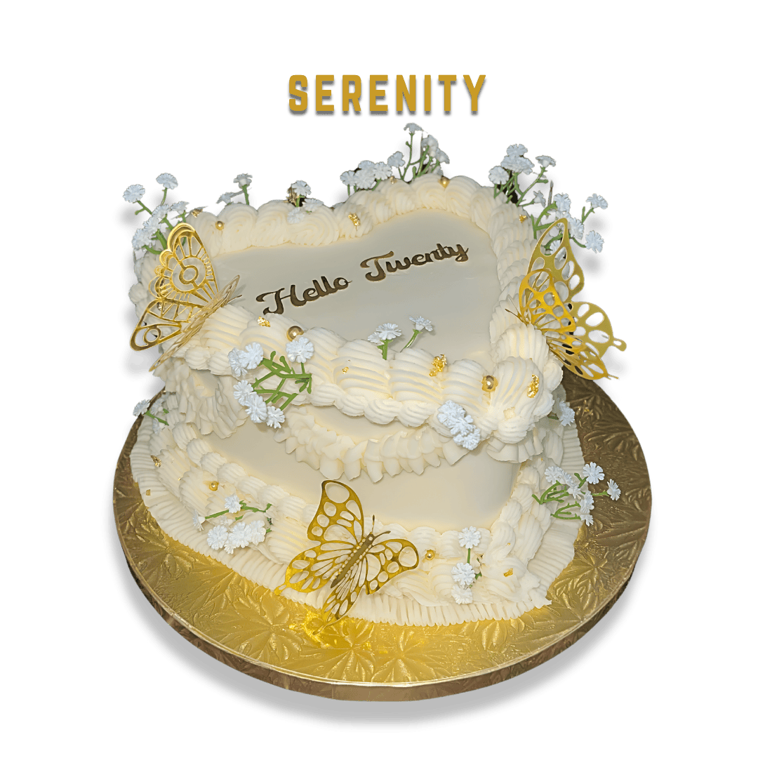 Serenity Cake
A white, heart-shaped cake decorated with white flowers, gold butterflies, and the word "SERENITY" on top, with the message "Hello Twenty" written in the center, placed on a gold cake board against a black background.