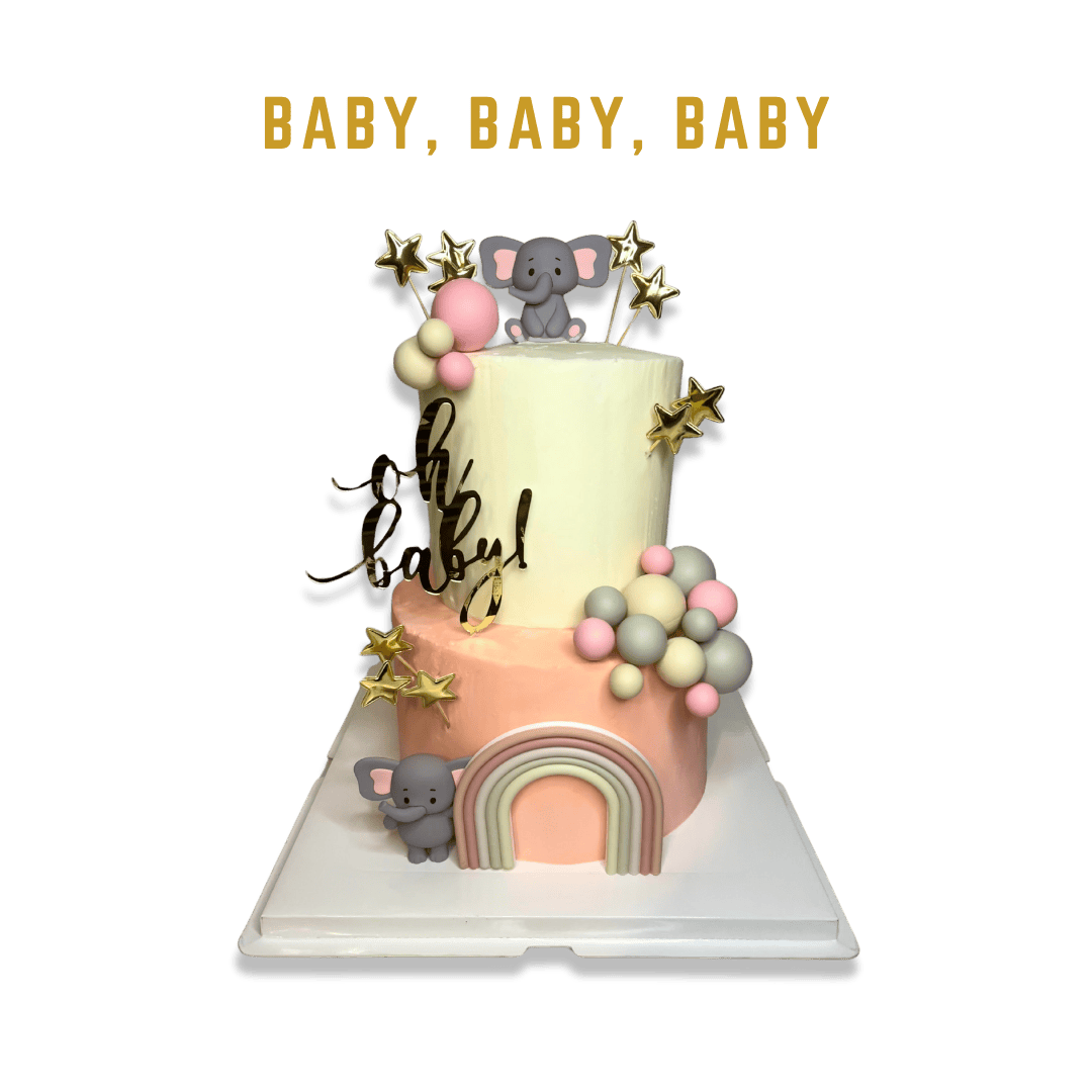 A two-tiered baby shower cake with pastel colors and a modern design. The bottom tier is peach-colored with a fondant rainbow and a small gray elephant figure at the base. The top tier is off-white, adorned with a second elephant figure, pastel ballo