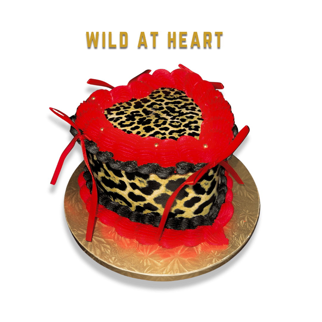 A cake with leopard print and red decorations, topped with a heart-shaped leopard print design and red pasta or fondant embellishments, with the text 'Wild at Heart' above it.
