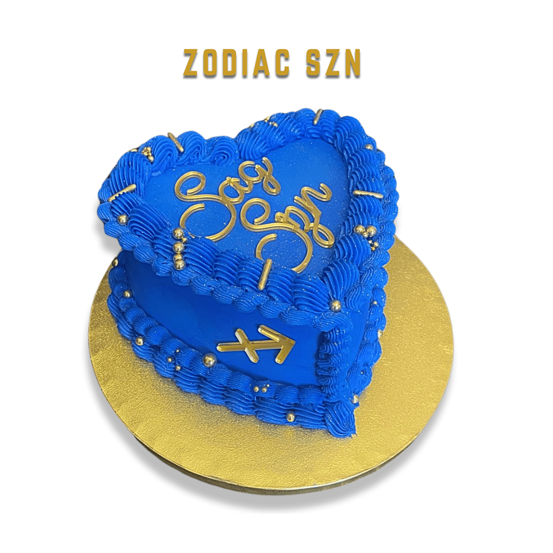 Blue heart-shaped cake with blue icing and gold decorations, including the word 'Love,' and astrology symbols for Gemini, on a gold base.