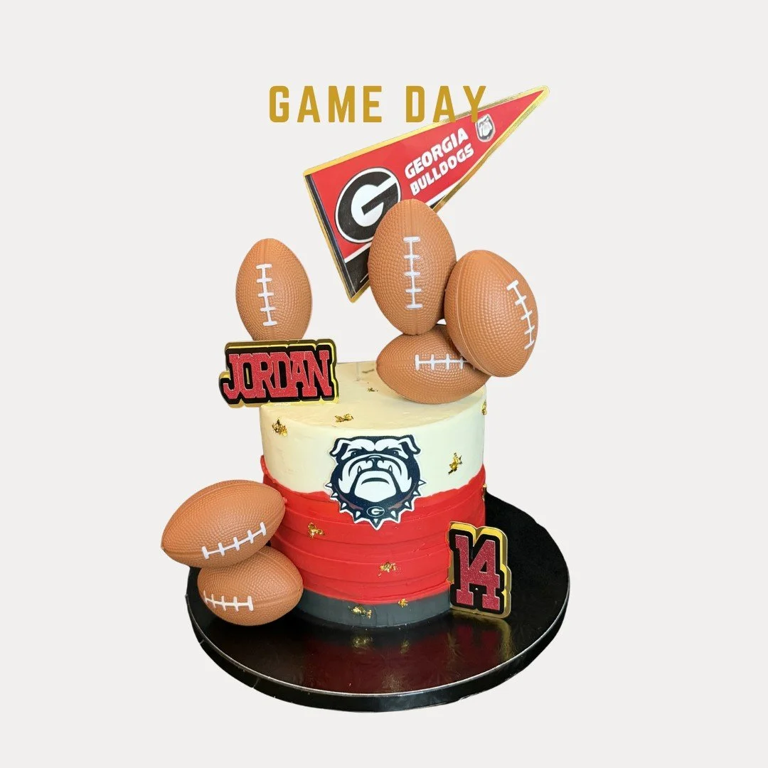 Game Day Cake is a birthday cake decorated with Georgia Bulldogs football theme. The cake has football-shaped decorations, a Bulldogs logo, and a flag, and the number 14.