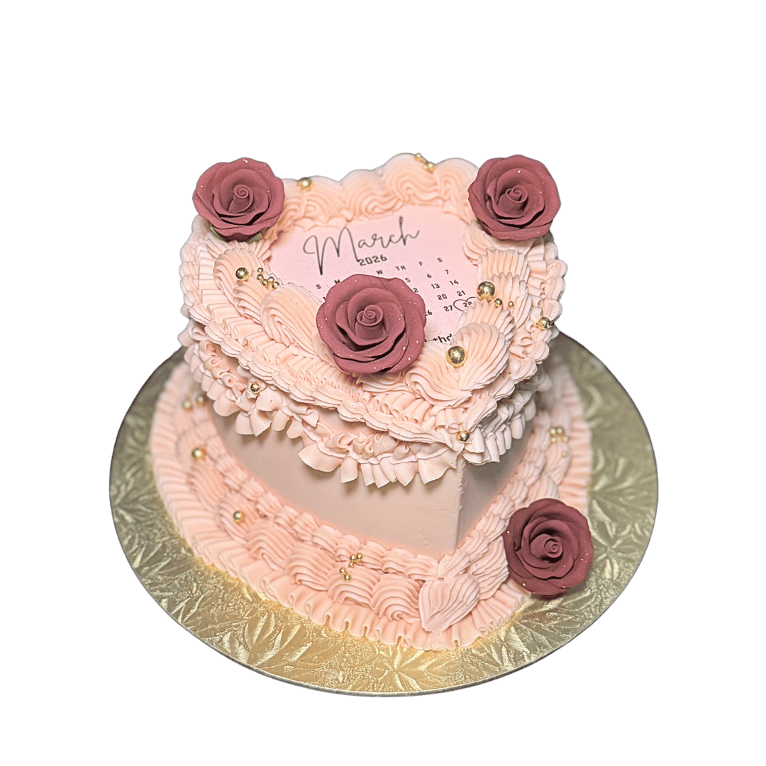 Pink heart-shaped birthday cake decorated with pink and purple roses, gold beads, and pink icing swirls, with a calendar marking March 2026 on top.