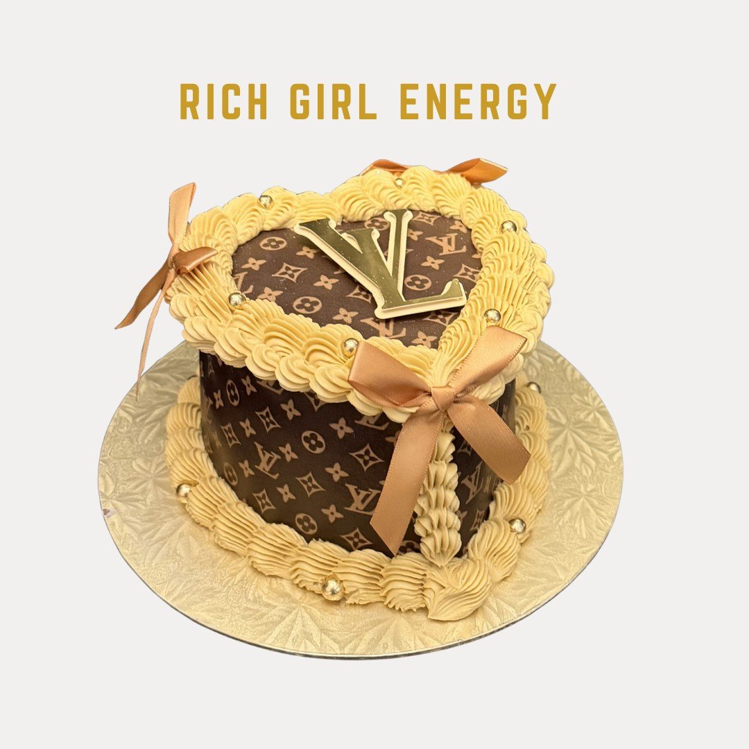 Rich Girl Energy Cake is a luxury cake designed with Louis Vuitton pattern, shaped like a clock with a gold "Y" and "L" on top, decorated with gold and beige icing and ribbons, on a gold cake board.