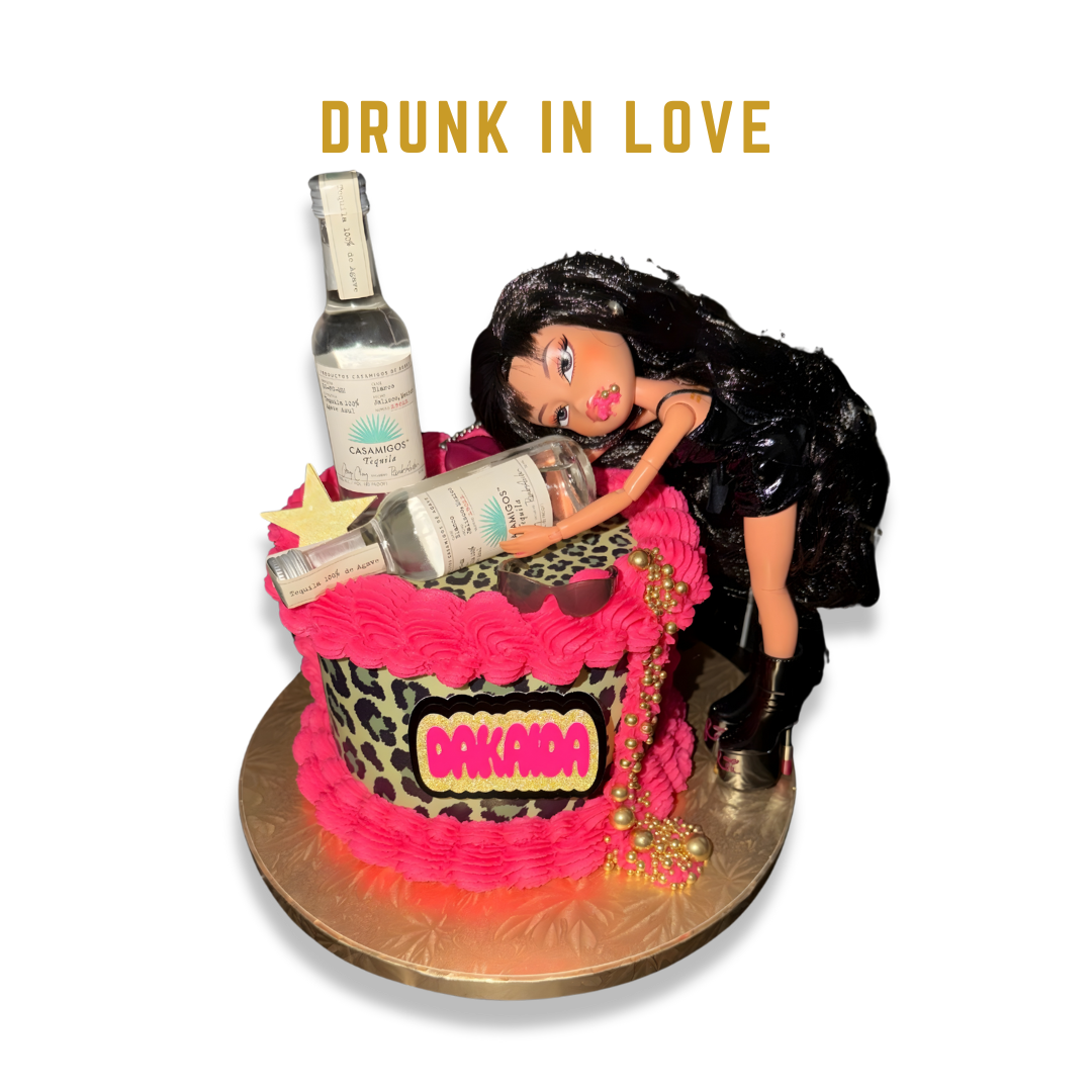 A decorative cake with leopard print design and pink frosting, topped with a doll figurine and two mini bottles of tequila, with gold beads and other ornaments.