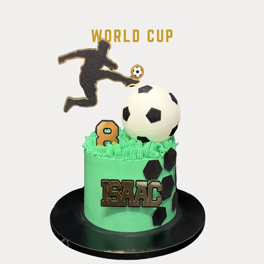 Green soccer-themed birthday cake with a large soccer ball decoration, smaller soccer ball on a figure kicking it, and black hexagon accents. The cake has a personalized name "ISAAC" and a number 8, with a silhouette of a soccer player on top and "WO