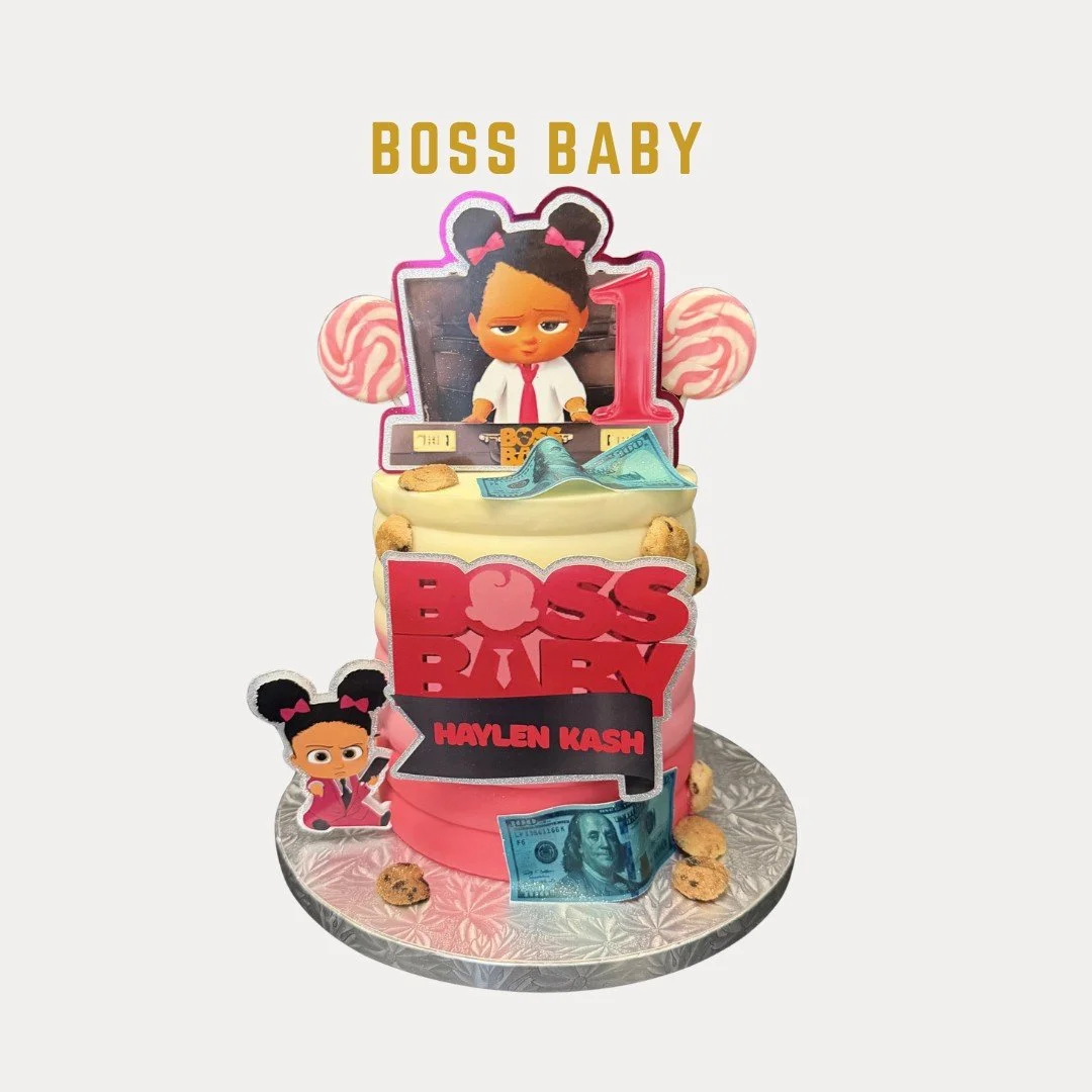 Birthday cake with a Boss Baby theme, featuring a cartoon figure of a baby in a suit with dark hair in buns, surrounded by decorations like pink candy, ten cookies, and fake money, with a large 'BOSS BABY' sign and a small photo of the character in t