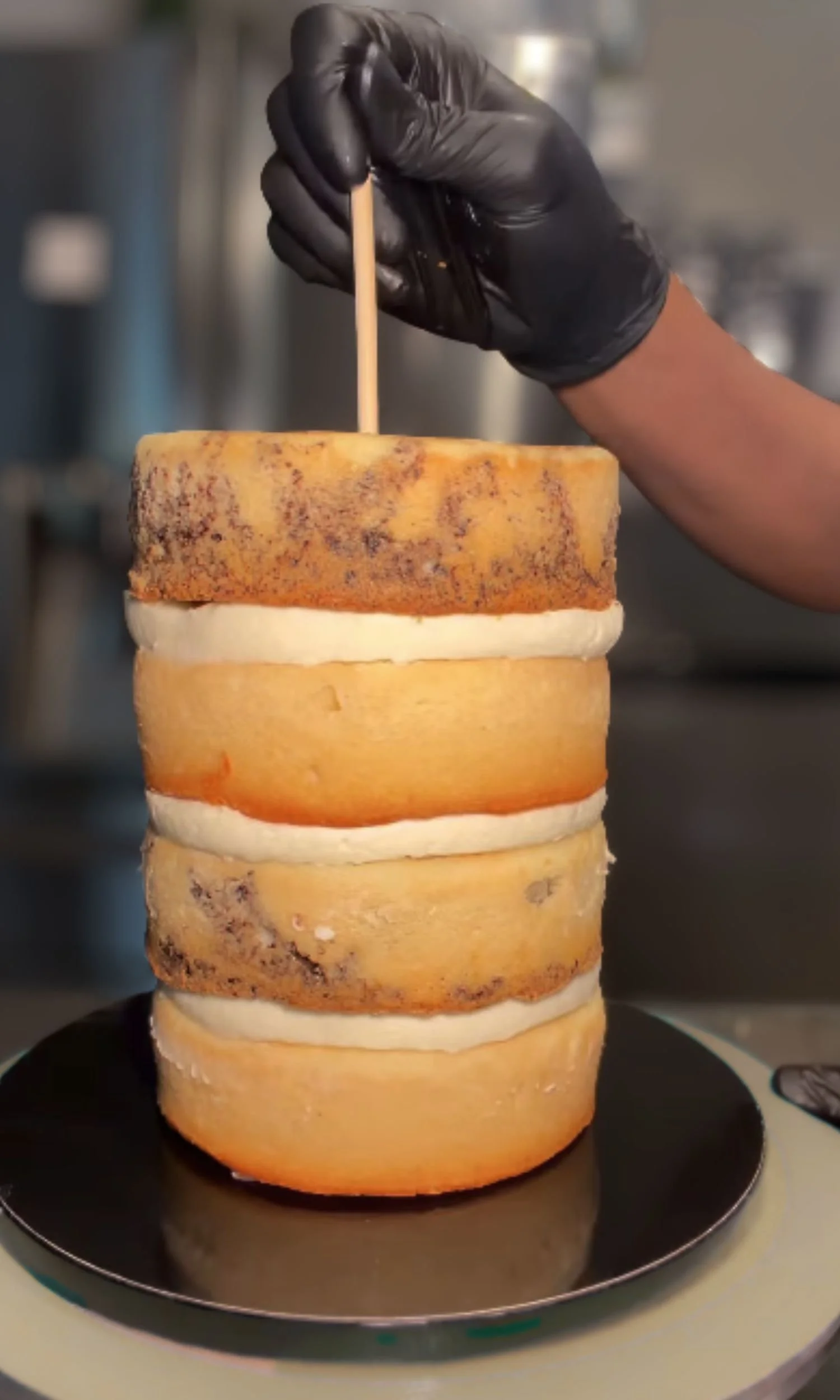 Stacked layers of cheese with a person wearing black gloves inserting a toothpick into the top layer.