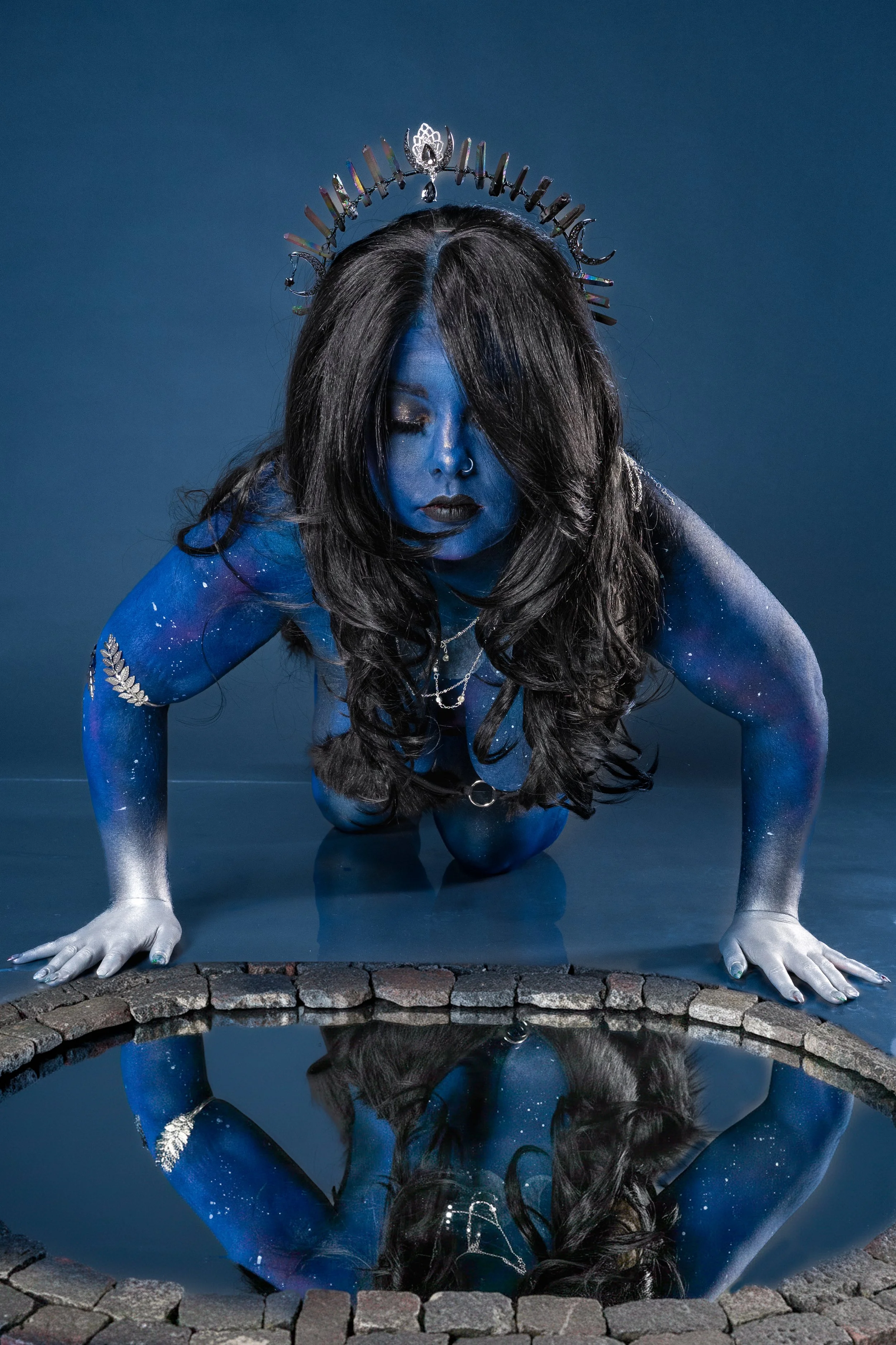 Portrait of model in blue body paint looking into a mirror