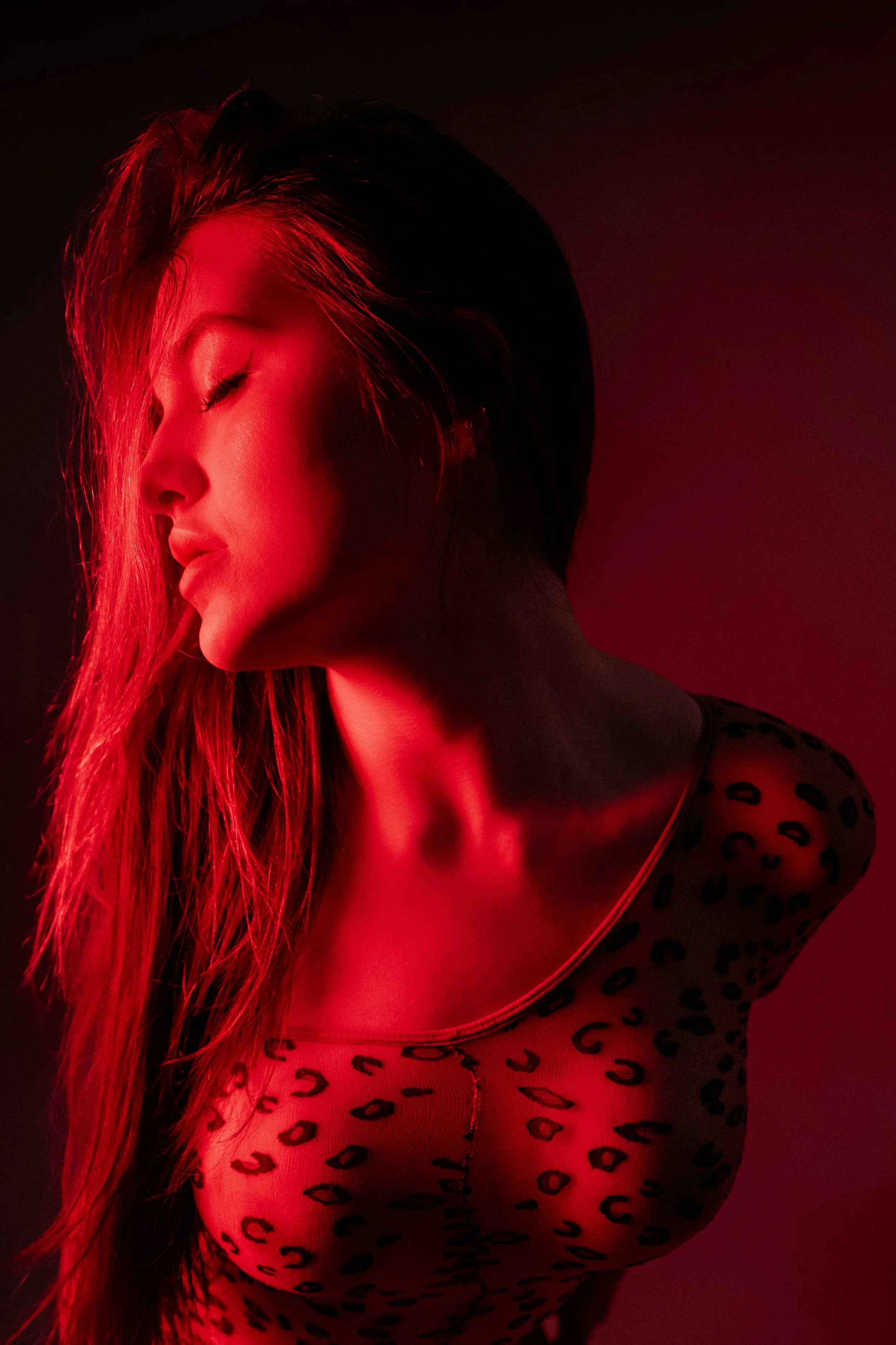 Portrait of a woman in a transparent leopard print body suit, in red lighting.
