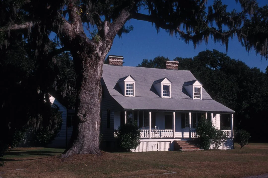 Historic Snee Farm in South Carolina, with a white plantation house behind a large oak draped in Spanish moss. The present house was built after the Pinckney family’s ownership of the indigo plantation.