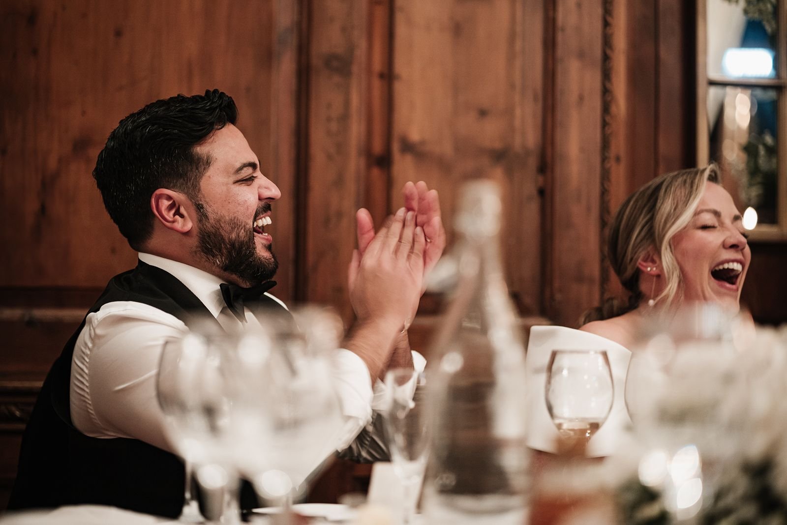 Groom clapping and bride laughing during wedding speeches