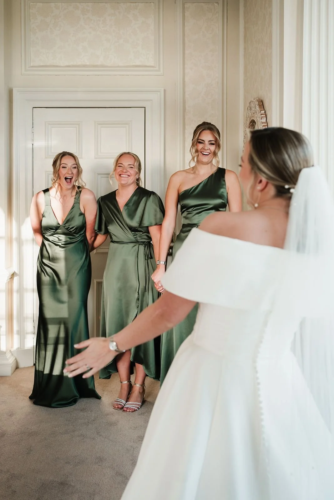 Bridesmaids in dark green dresses smiling at bride during first look