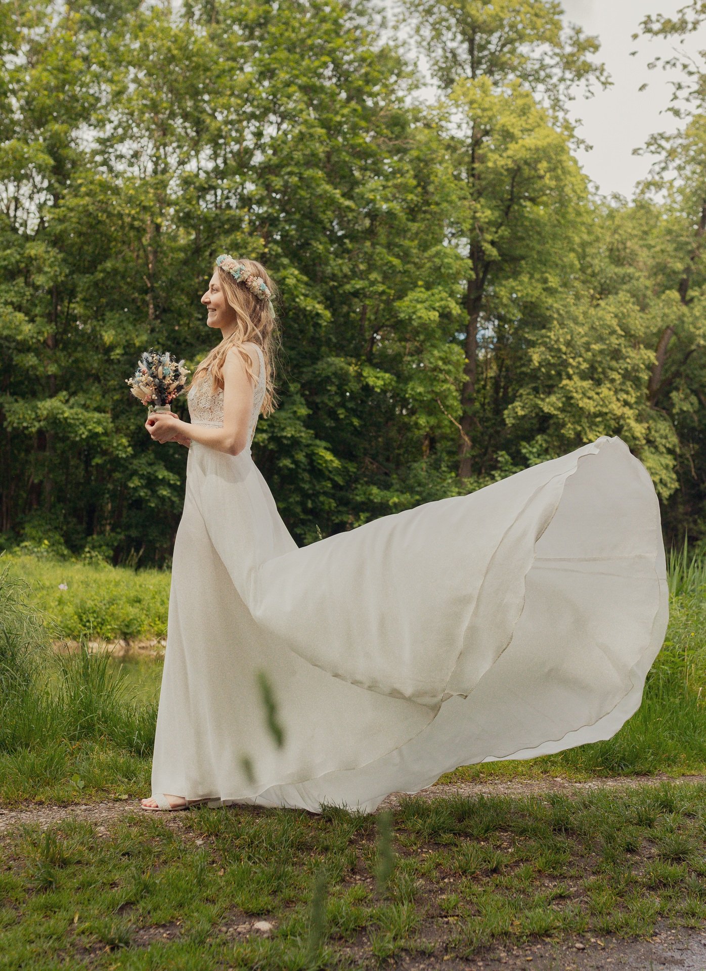 Braut im weißen Kleid mit Blumenstrauß im Grünen