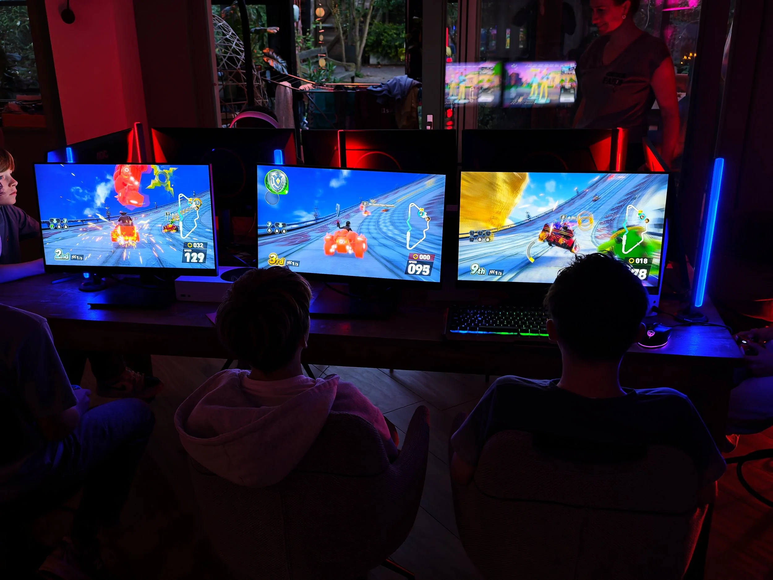 Kinderen spelen een racespel op drie computers met kleurrijke racing games in een donkere ruimte met neonlichten.