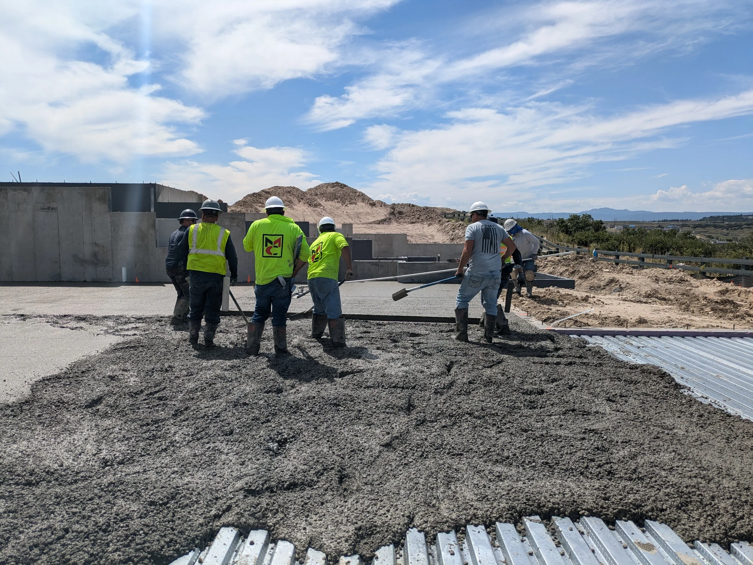 Workers pouring concrete for a structural floor in Colorado with mountains and a blue sky