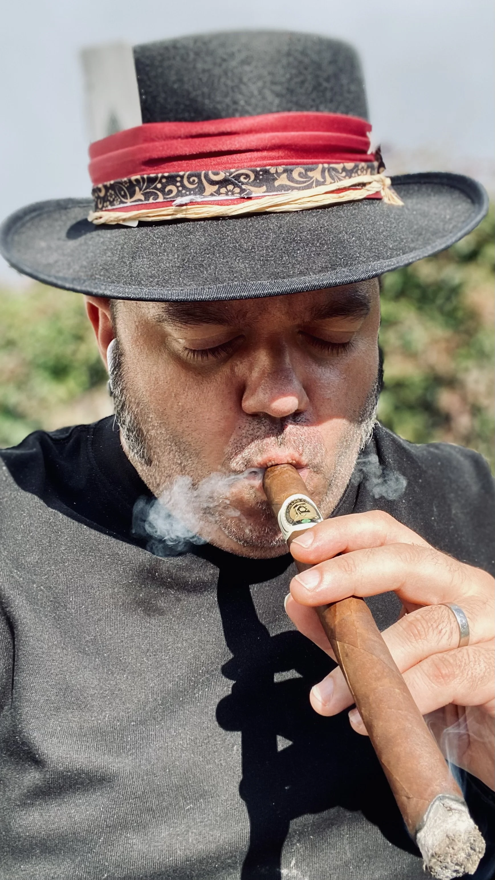 Julyo is wearing a stylish hat and smoking a cigar.