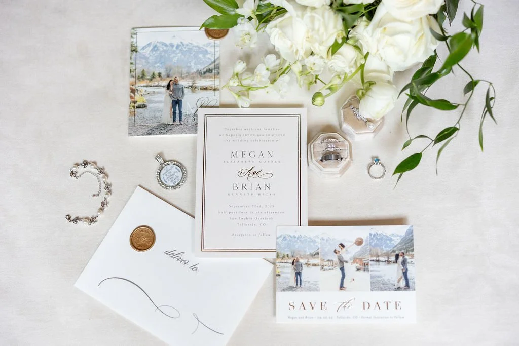 Flat lay of invitation, save the date, wedding rings, engagement ring, bride's jewelry, and bride's bouquet 