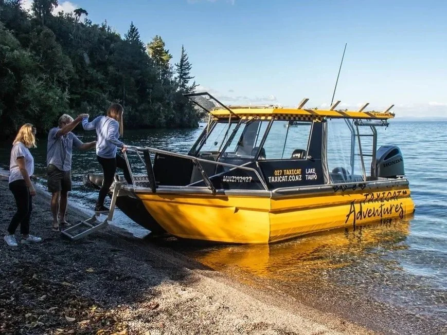 Four people boarding a yellow boat named 'Adventures' on a lakeshore with trees in the background.