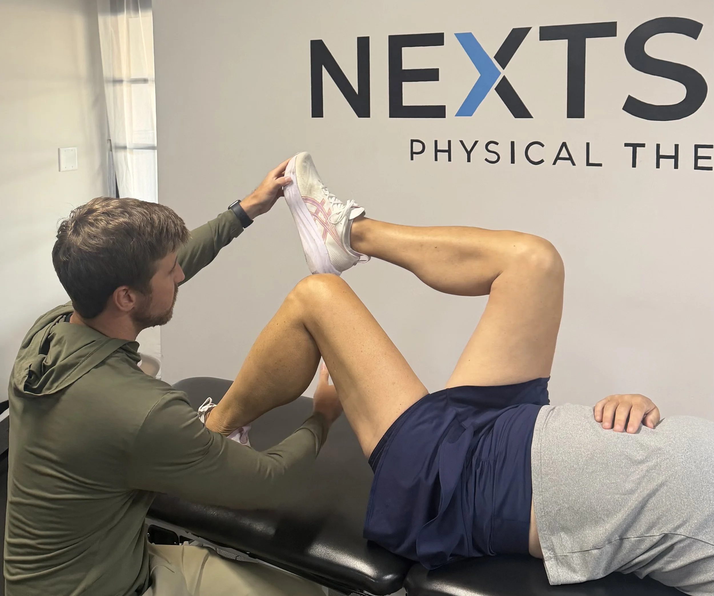A physical therapist or trainer assisting a person with leg stretches in a medical or therapy setting.