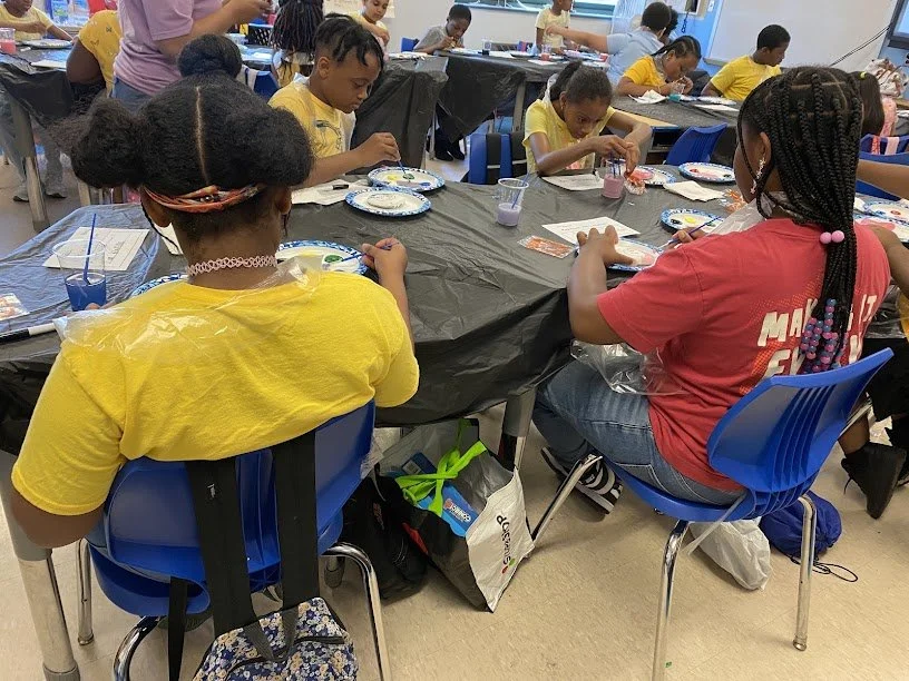 Children participating in an art activity at a classroom table with painting supplies.
