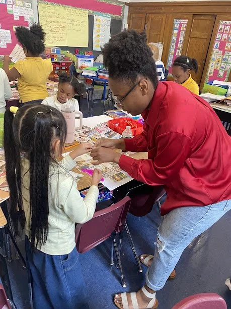 A teacher assisting students with activities at their desks in a classroom.