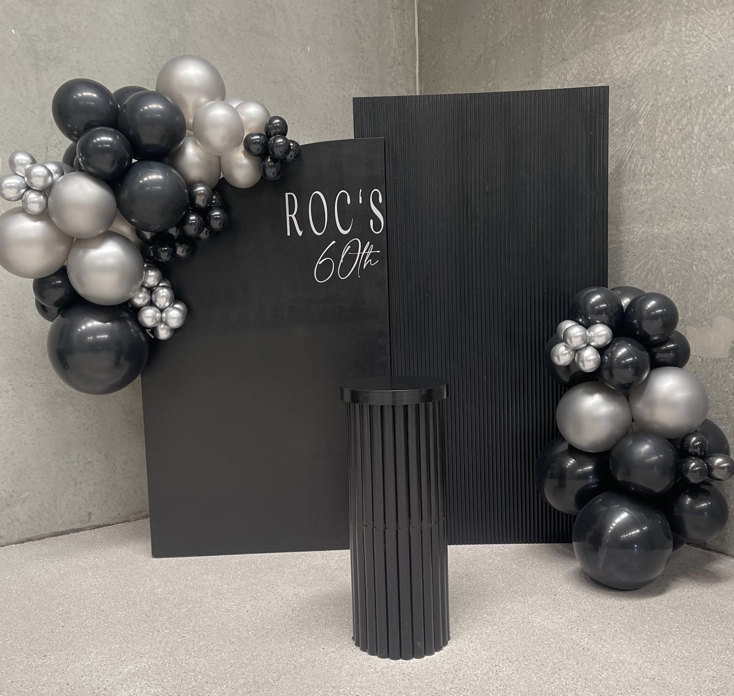 Black backdrop decorated with black, silver, and pearl balloons for a celebration, with the text 'ROC'S 60th' written on it.