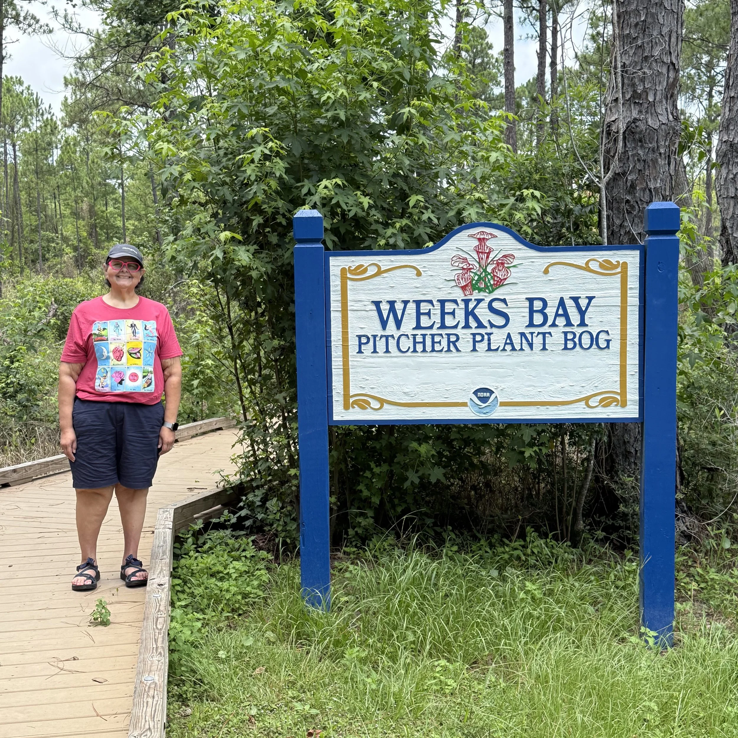 a smiling woman next to a sign in a park