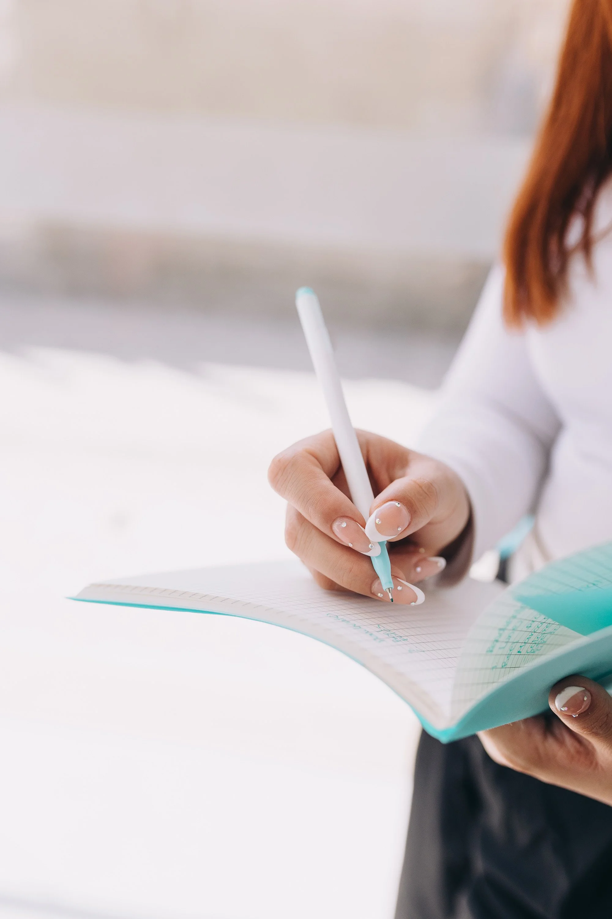 A person holding a pen and writing in a notebook with grid paper.