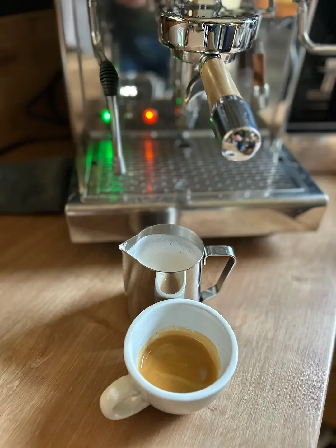 Eine Cappuccinotasse und ein Milchkännchen mit aufgeschäumter Milch stehen vor einer Siebträgermaschine