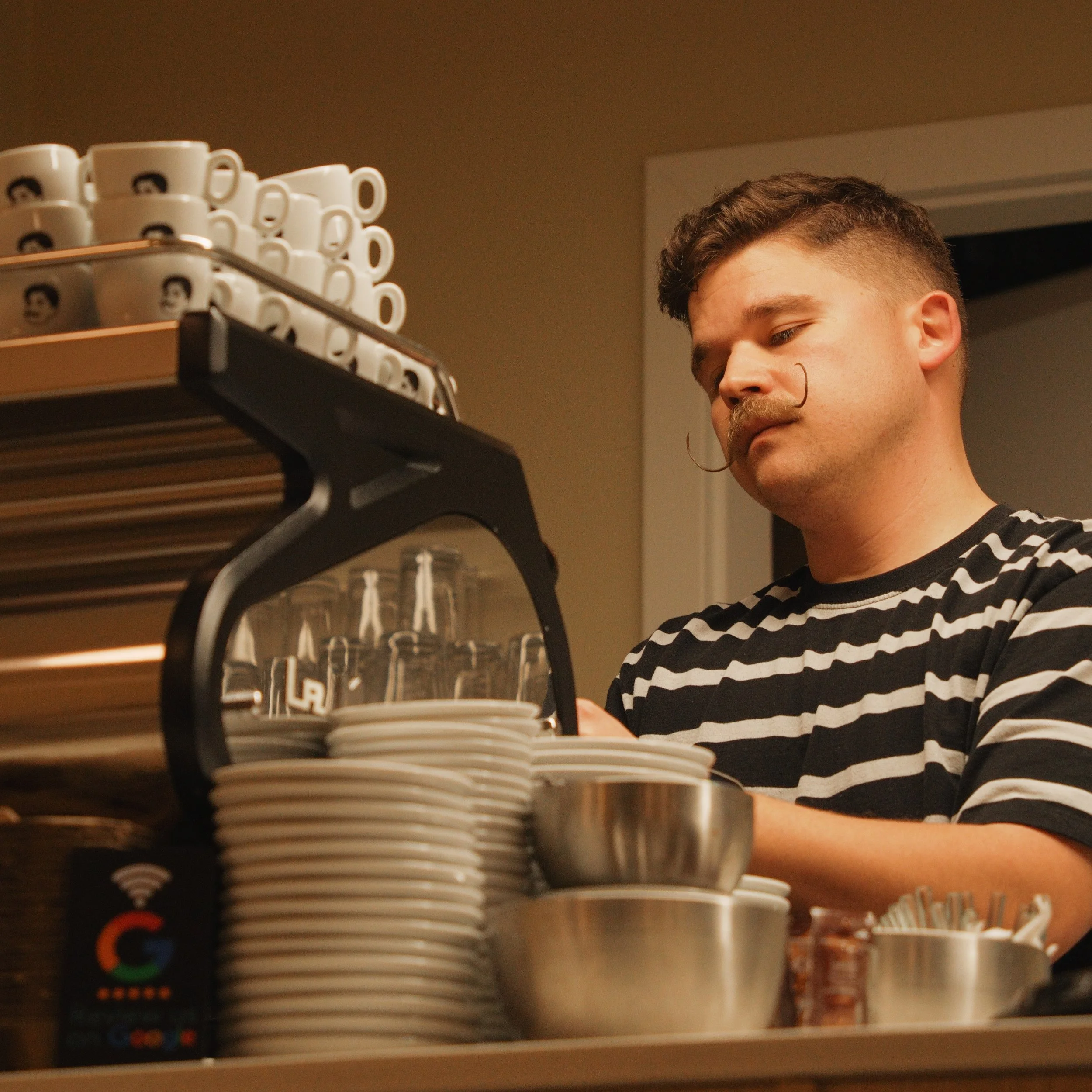 Matej. A barista with short dark hair and a mustache making coffee.