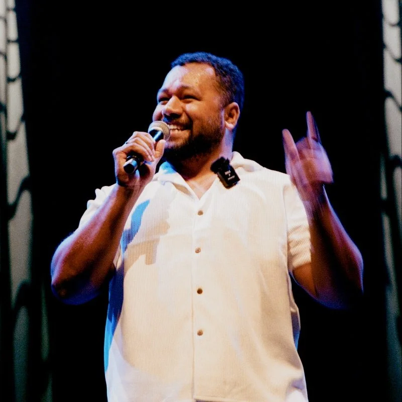 Person speaking on stage with microphone, smiling.