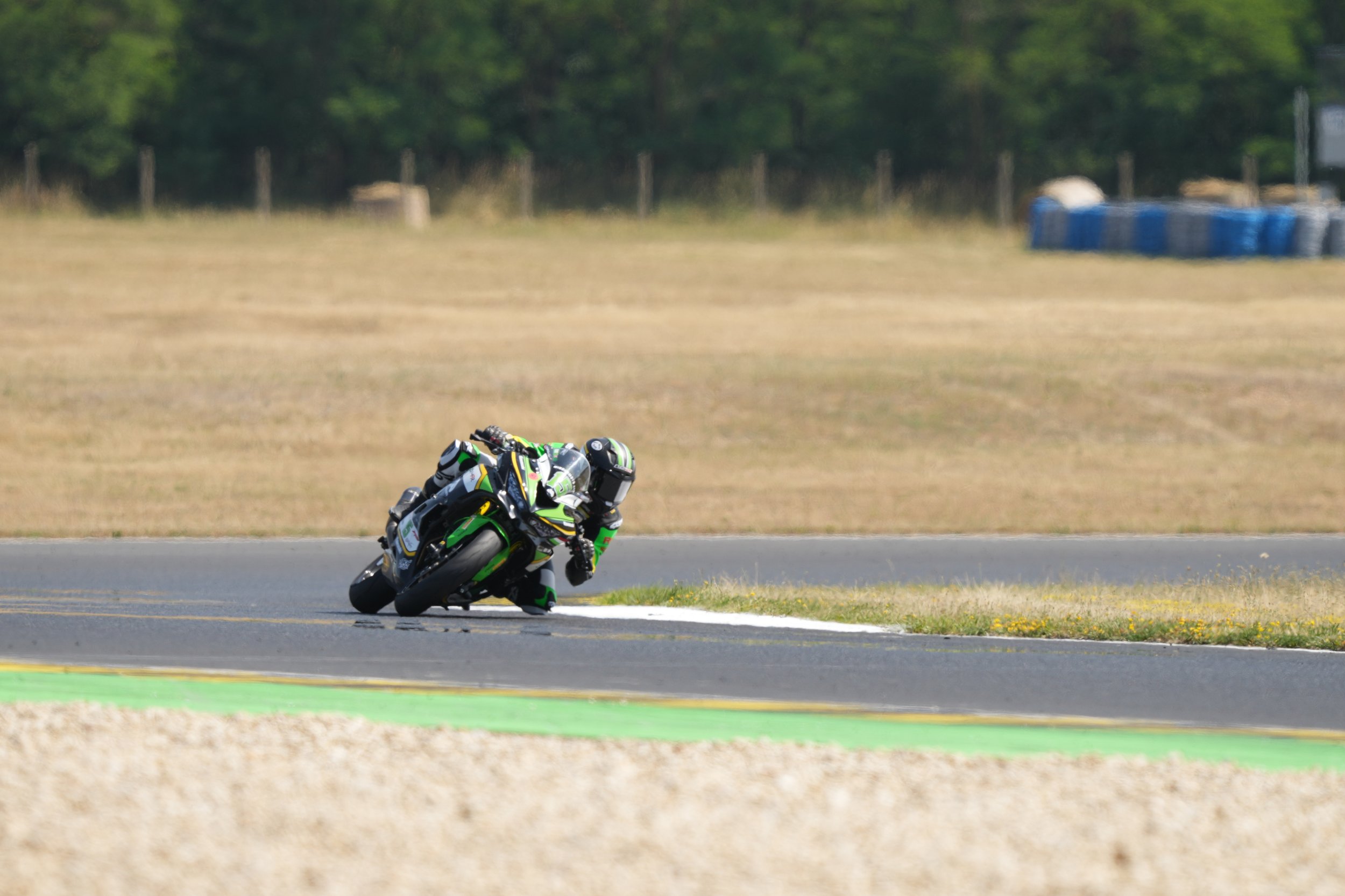 A motorcyclist in black and green gear leaning into a turn on a racetrack.
