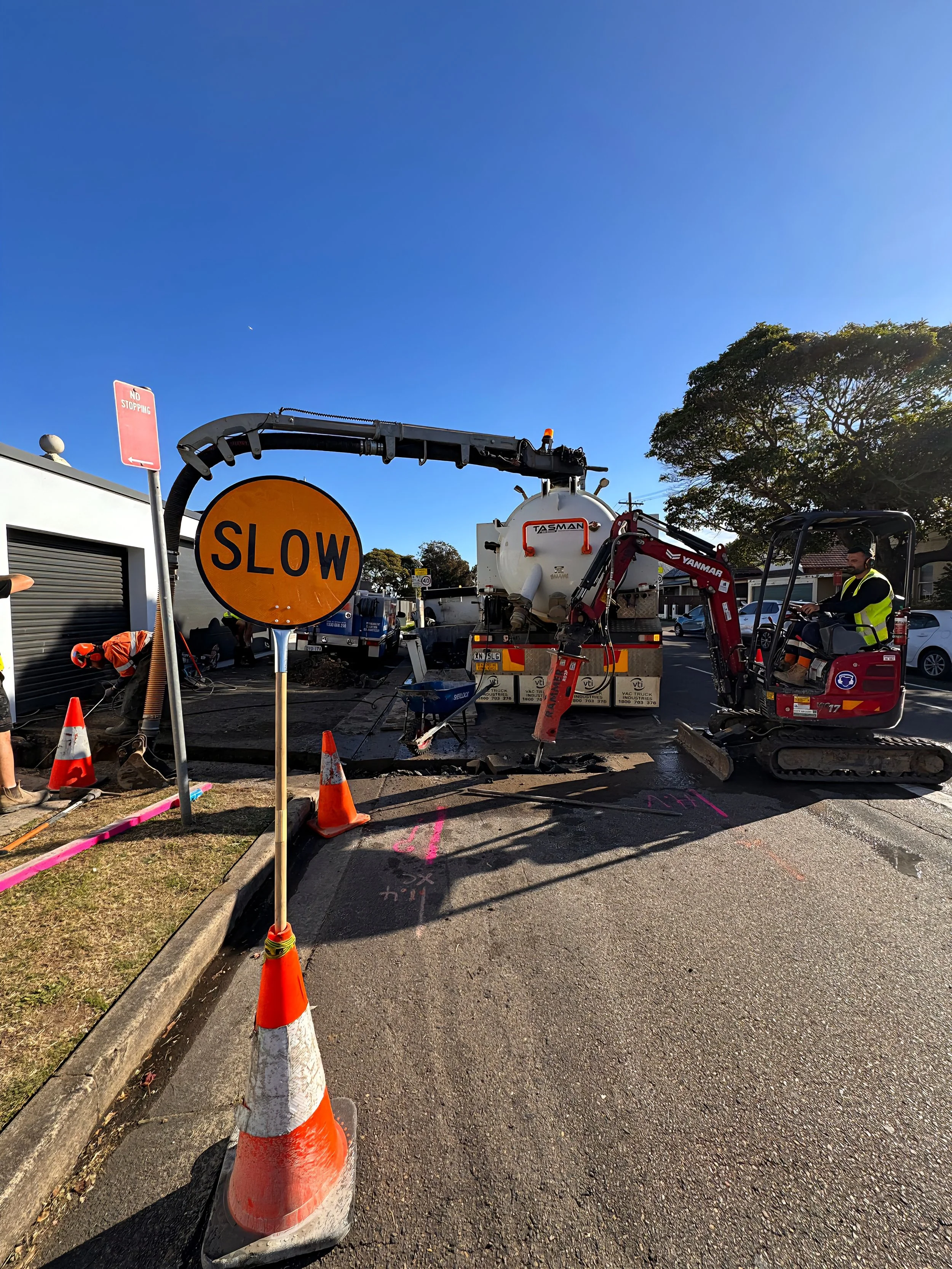 Construction workers, traffic control and excavator on a road civil site digging trenches in Sydney