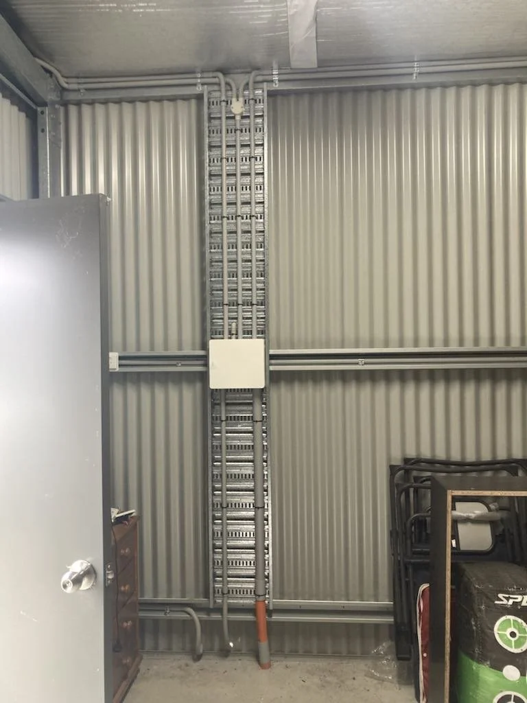 Interior of industrial room with metal wall and door, large electrical conduit system, stack of chairs, storage items.