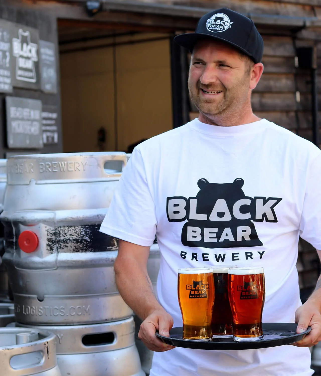 Man with Black Bear Brewery hat and t-shirt on holding three pints of beer on a tray