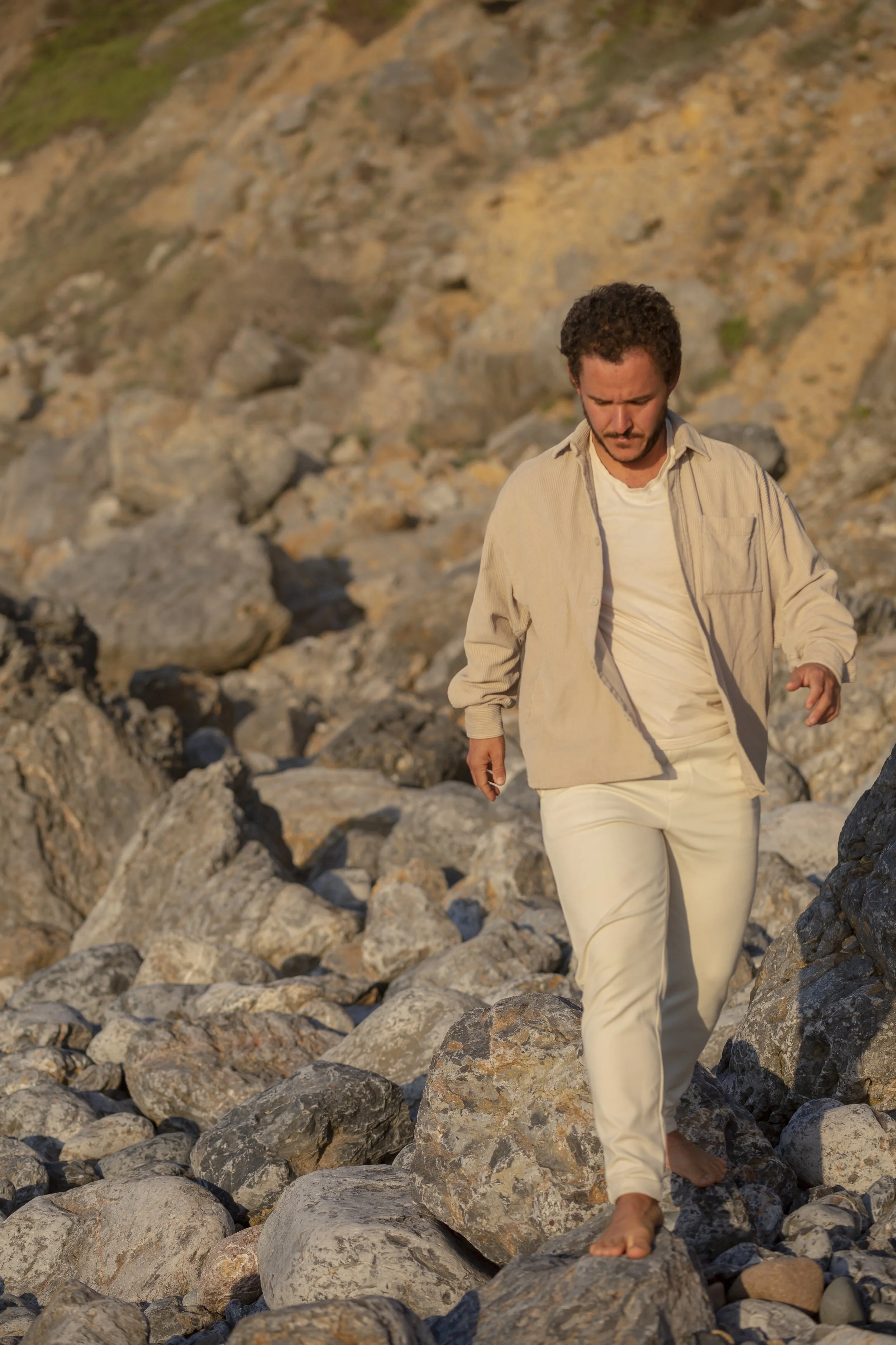Pedro walking mindfully across beach stones with ocean cliff behind him, demonstrating embodied presence