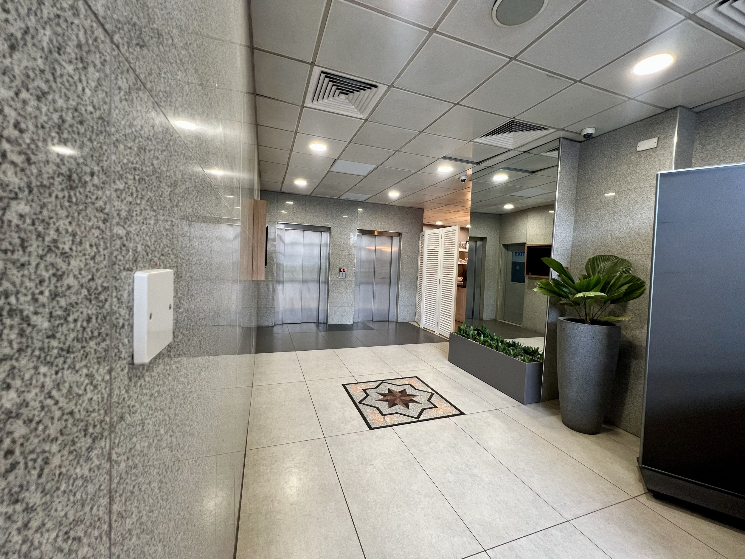 Lobby with two elevators, potted plant, decorative tile floor, and a white storage cabinet.