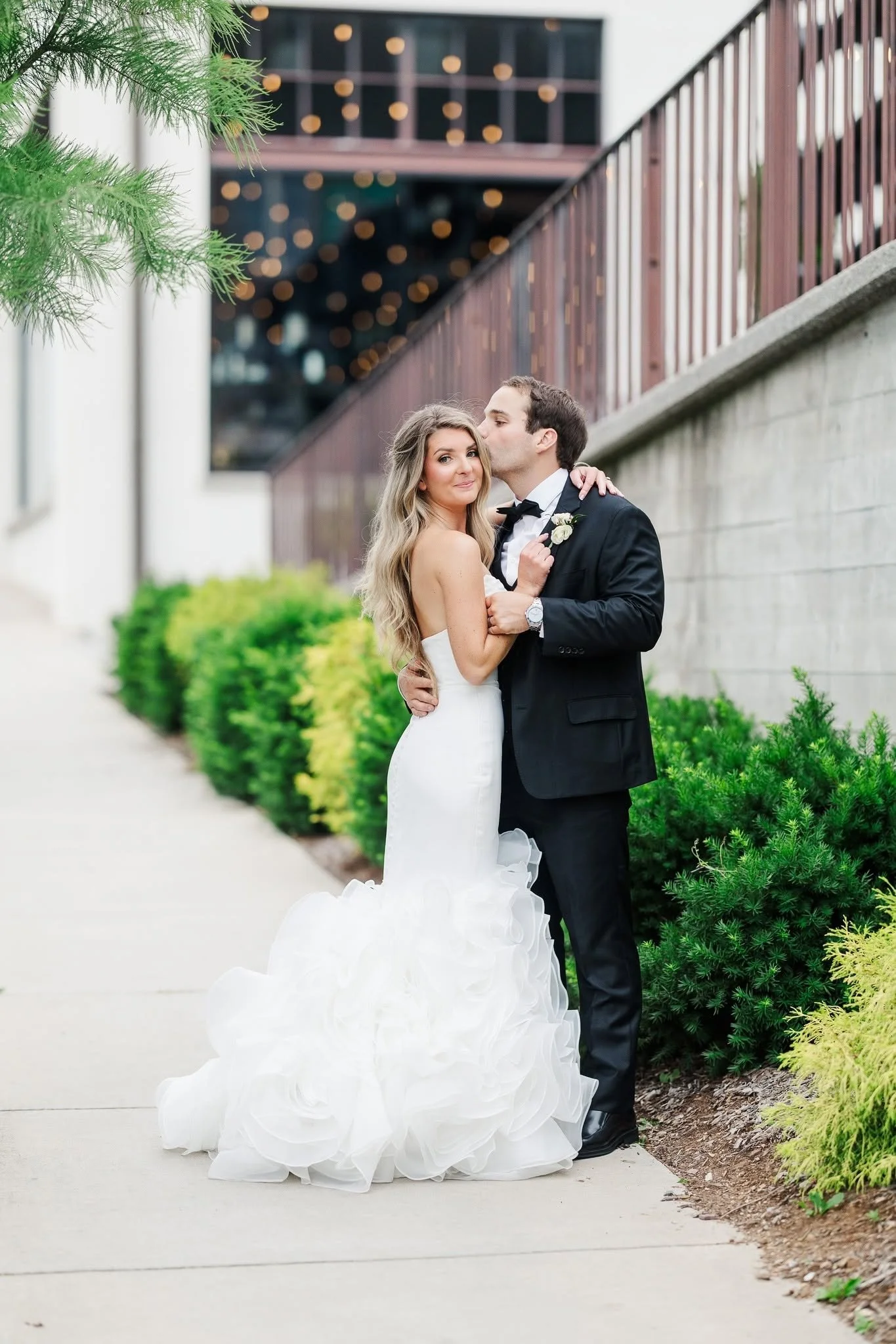 Bride and groom posing outside The Press Room in Knoxville on their wedding day, with the historic event venue and greenery in the background.