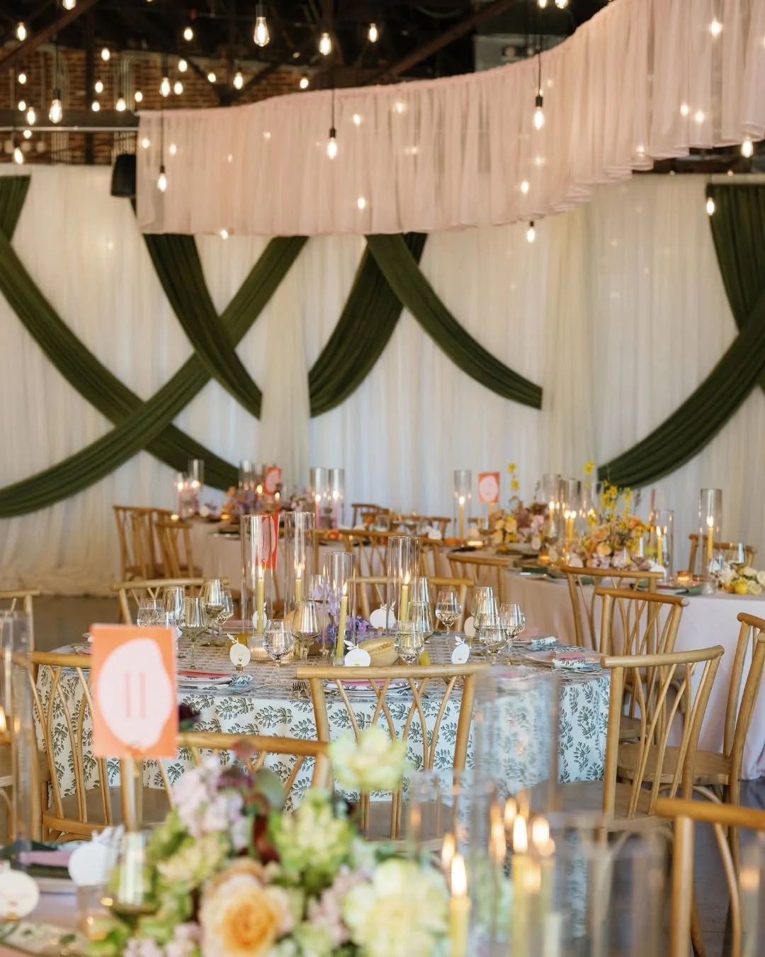 Wedding reception setup at The Press Room in Knoxville featuring floral centerpieces, candlelight, patterned linens, wooden chairs, and elegant draping.