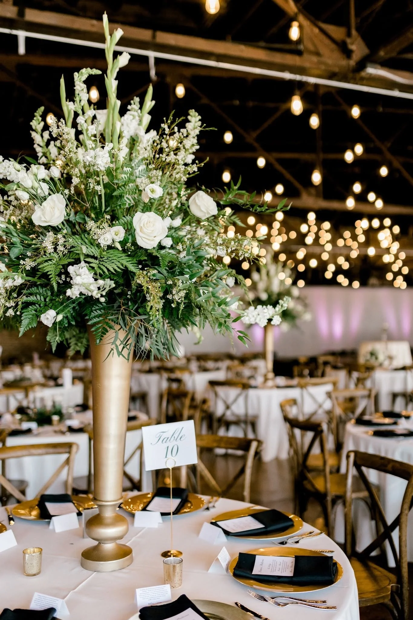 Wedding reception at The Press Room in Knoxville featuring elegant white floral centerpieces, gold accents, and warm string lights inside the historic event venue.