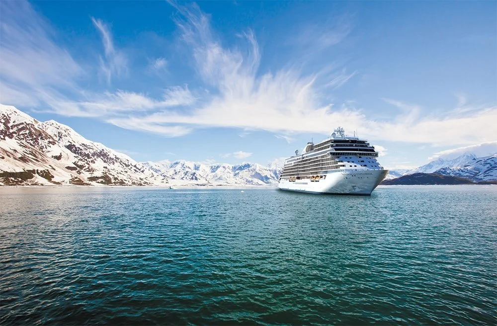 Large white cruise ship sailing in icy waters near snow-covered mountains under a partly cloudy sky.